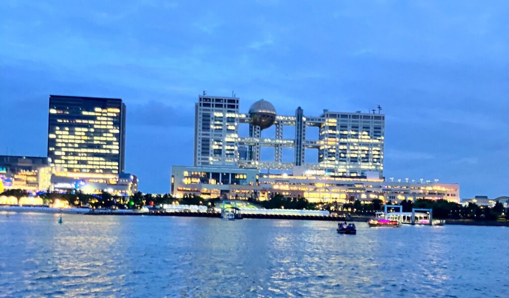 夕暮れの海越しに見える、明かりが灯ったフジテレビ本社と周辺のビル群